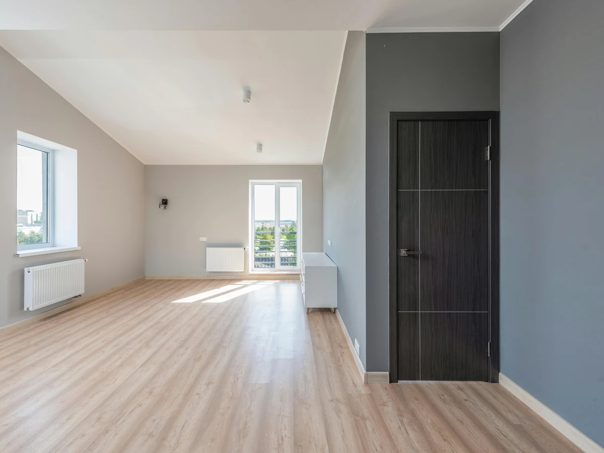 interior-painting-empty-grey-room-york-painters-2 A freshly painted empty room with grey and white walls, a dark door and a light wood floor