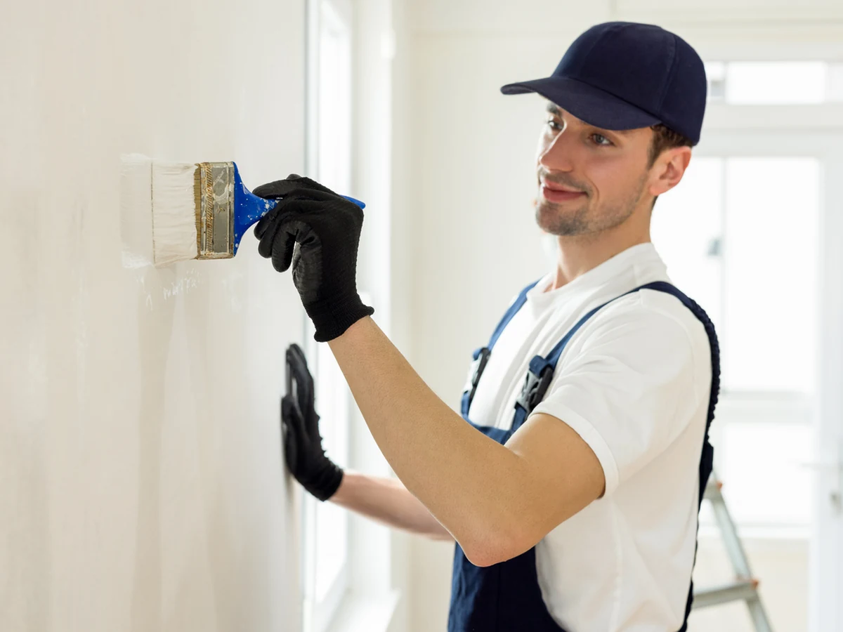 painting-decorating-young-male-painter-york-painters A young painter in a cap and black gloves brushing paint onto a white wall